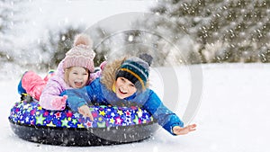 Active toddler girl and school boy sliding together down the hill on snow tube. Happy children, siblings having fun