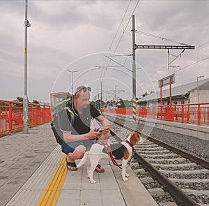 Active tourist with backpack using phone and waiting for train. Man and beagle dog waiting on railway station. Older