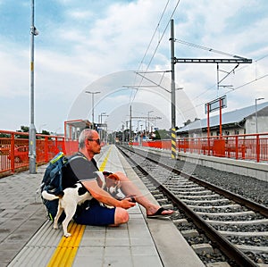 Active tourist with backpack using phone and waiting for train. Man and beagle dog waiting on railway station. Older