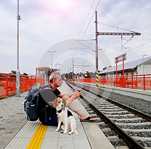 Active tourist with backpack using phone and waiting for train. Man and beagle dog waiting on railway station. Older