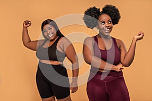 Active two plus size women after training in fashionable sporty clothes posing together, smiling. Gym, healthy lifestyle concept