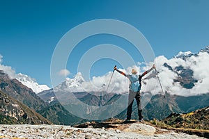 Active vacations concept image. Young hiker backpacker man rising arms with trekking poles enjoying the Thamserku 6608m mountain