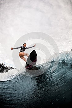 Active woman in black wetsuit professionally rides on surf board on wave photo