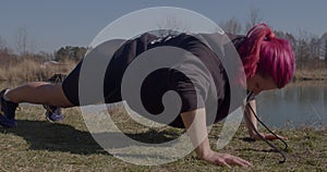 Active woman doing push-ups from the ground on river. She holds body, bends her arms elbow.