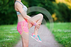 Active woman doing warm-up routine in the park before running, stretching leg muscles with standing single knee to chest