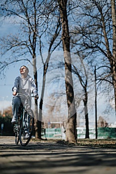 Active woman enjoying a relaxing bike ride in sunny park with bare trees.