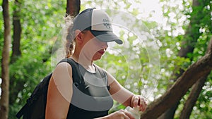 Active woman hikes through rocky grotto in rich forest, pauses hydration break. Adventurer drinks from reusable soft