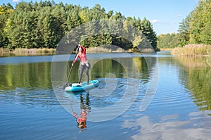 Active woman paddling SUP board on beautiful lake, autumn forest landscape and nature on background, stand up paddling