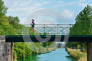 Active woman runner jogging across river bridge, outdoors running