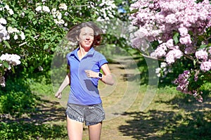 Active woman runner running in spring park with lilac blossom, morning run outdoors, fitness jogging healthy lifestyle