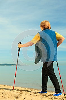Active woman senior nordic walking on a beach. from behind