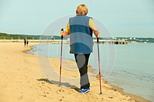 Active woman senior nordic walking on a beach. from behind