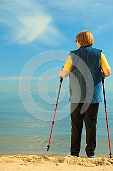 Active woman senior nordic walking on a beach. from behind