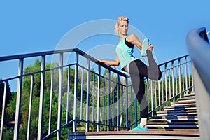 Active woman stretching her leg standing on bridge steps