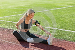 Active woman stretching on a sunny outdoor track field wearing fitness apparel