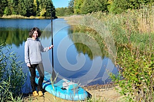 Active woman with SUP board near beautiful lake, nature on background, stand up paddling water adventure