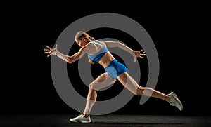 Active woman, track athlete training isolated over black studio background.
