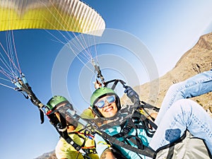 Active young adult people woman enjoy paraglide activity fliying in the sky with professional pilote in the back - cheerful happy