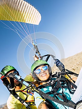 Active young adult people woman enjoy paraglide activity fliying in the sky with professional pilote in the back - cheerful happy