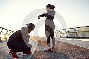Active young african couple, man and woman in sport clothing tying shoelaces, preparing before jogging outdoors. Morning