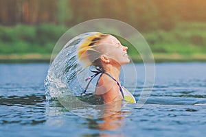 Active young blonde woman waving hair splashing water in river. Beautiful healthy lady relax and laughing, raising head