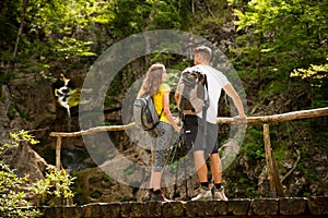 Active young cople hiking on a wooden brifge over mountain creek