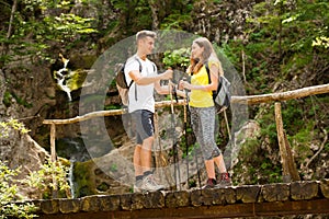 Active young cople hiking on a wooden brifge over mountain creek