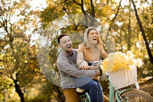 Active young couple enjoying riding bicycle in golden autumn par