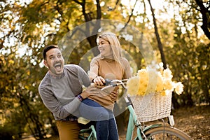 Active young couple enjoying riding bicycle in golden autumn par