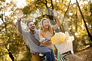 Active young couple enjoying riding bicycle in golden autumn par