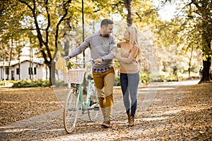 Active young couple enjoying romantic walk with bicycle in golden autumn park