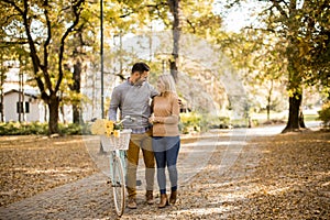 Active young couple enjoying romantic walk with bicycle in golden autumn park