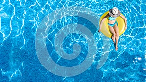Active young girl in hat in swimming pool aerial top view from above, child relaxes and swims on inflatable ring donut