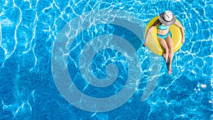 Active young girl in swimming pool aerial top view from above, child relaxes and swims on inflatable ring donut and has fun