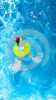Active young girl in swimming pool aerial top view from above, child relaxes and swims on inflatable ring donut and has fun