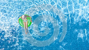 Active young girl in swimming pool aerial top view from above, child relaxes and swims on inflatable ring donut and has fun