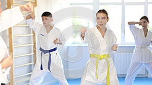 Active young girl wearing kimono training karate techniques in group during workout session