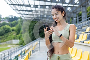 Active young indian woman with fitness bracelet using smartphone at stadium