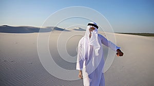 Active young male emirate Arabian UAE Sheikh rejoices in life and walks through expanses of desert on clear evening.