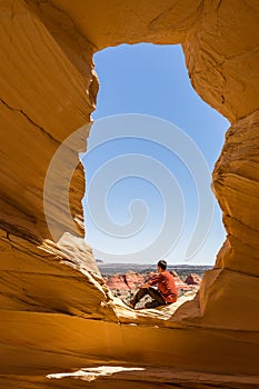 Active young man, contemplative hiker resting in the sunlight under an arch in Utah. Looking out over the desert landscape