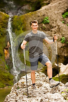 Active young man hiking in mountains near waterfall on a creek
