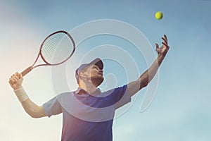 Active young man playing tennis outdoors. serve the ball against blue sky