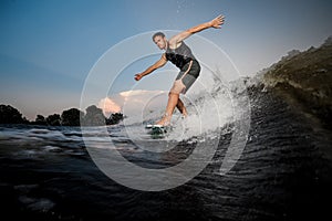 Active young man riding down the river waves in evening