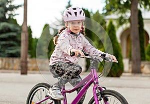 Active young school age girl, child riding a bike in a helmet, closeup. Kid rides a bicycle on a sunny day. Hands on handlebars