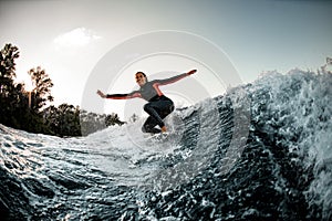 Active young wet woman in wetsuit balanced on surfboard and rides on the wave.