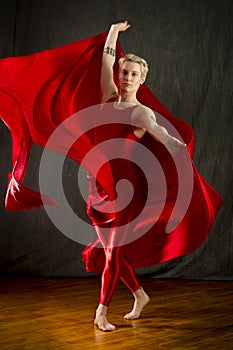 Young woman in red unitard swirling red fabric in studio.