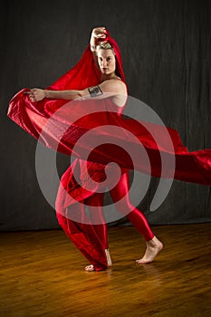 Young woman in red unitard swirling red fabric in studio.