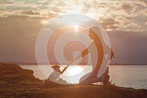 Active young woman dog trainer give hand to dog chihuahua paw sitting near sea summer sunset during obedience friendship training