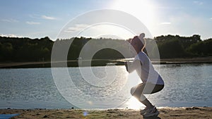 Active young woman doing exercise on sunset beach, the sun glare from the water. Athletic female in sportswear enjoying