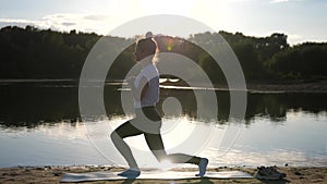 Active young woman doing exercise on sunset beach, the sun glare from the water. Athletic female in sportswear enjoying